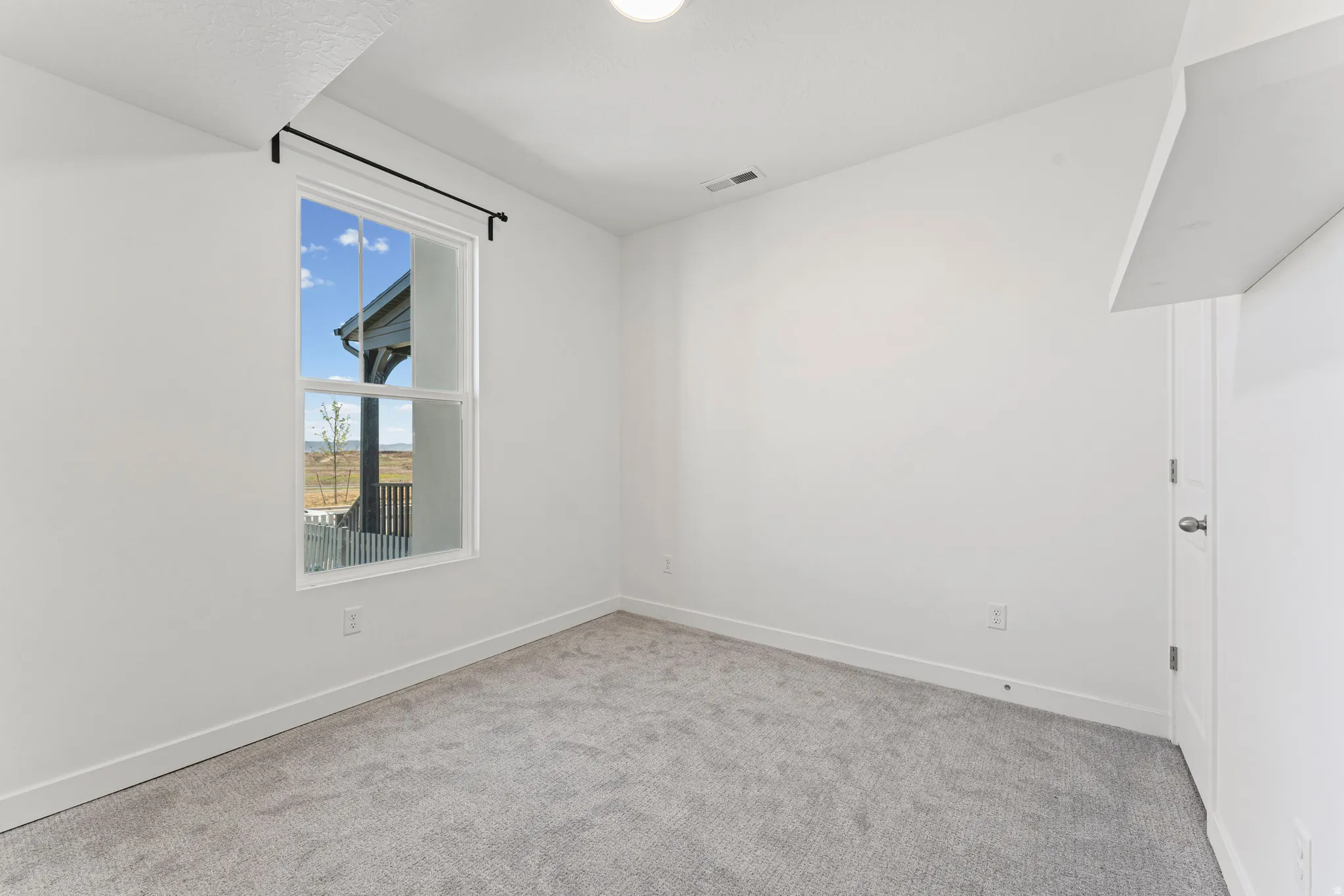 Bright interior space featuring a large window, light gray carpeting, and white walls