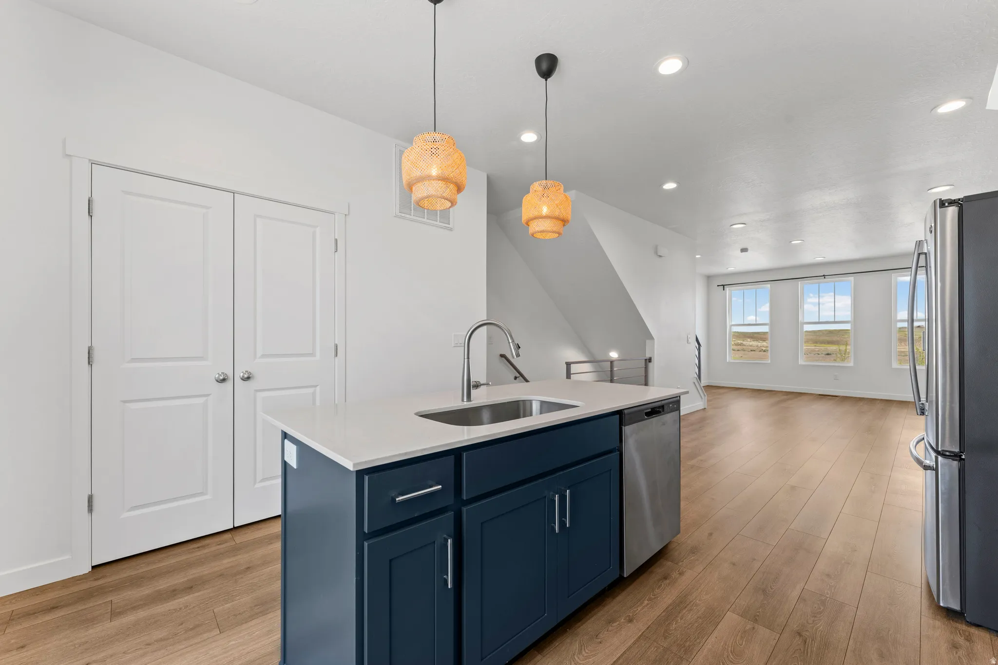 Open-concept living space featuring wood-finish flooring, a kitchen island with a single-basin sink, navy cabinetry, a stainless steel dishwasher, and recessed lighting