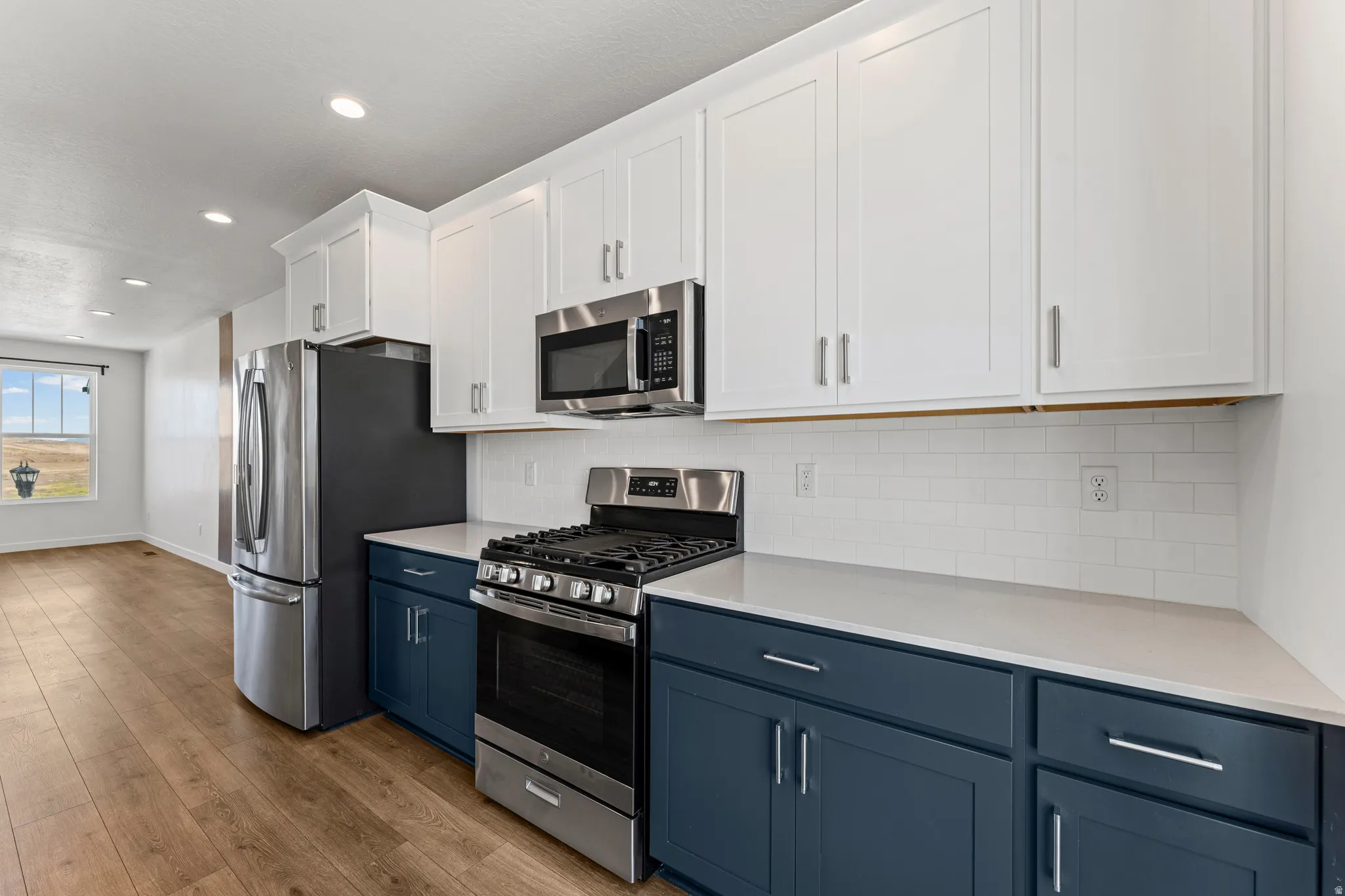 Modern kitchen featuring two-tone cabinetry with white upper and blue lower cabinets, stainless steel appliances, a subway tile backsplash, and light-toned countertops