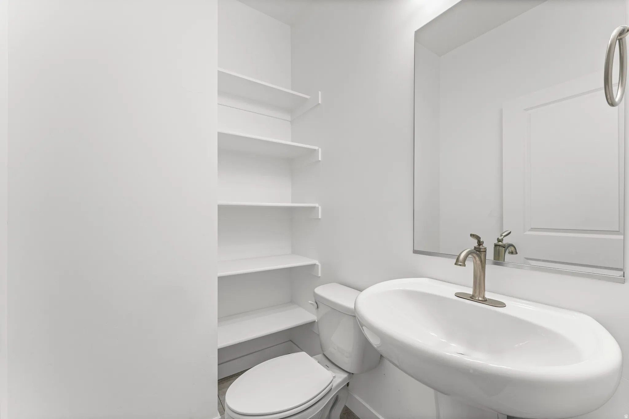 Contemporary bathroom featuring a pedestal sink with a brushed nickel faucet, a frameless wall mirror, and integrated shelving