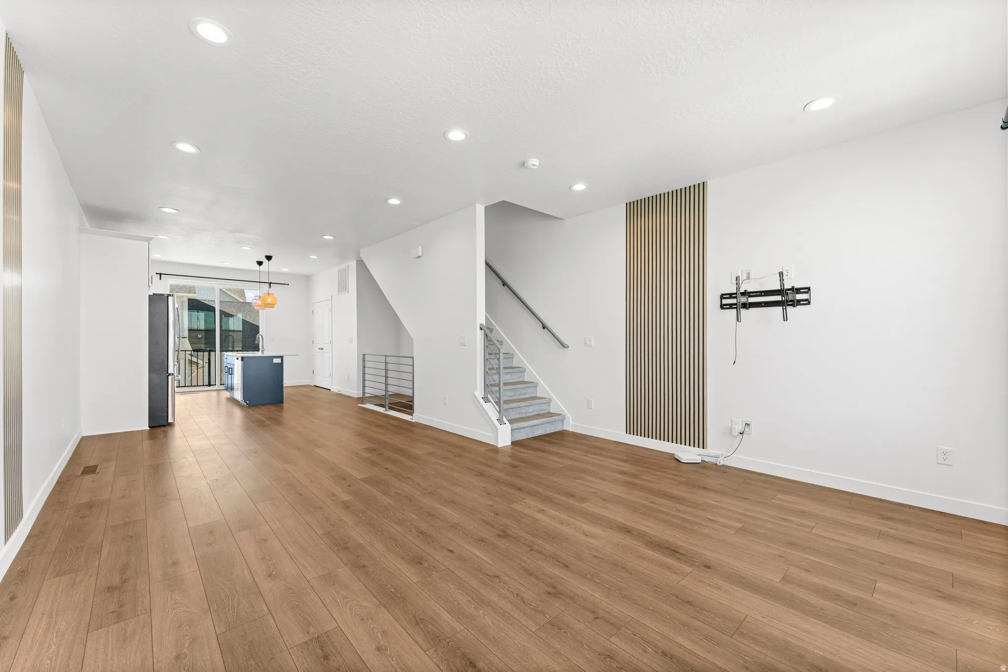 Open-concept living space featuring wood-finish flooring, recessed lighting, a contemporary kitchen island with pendant lights, and a staircase with metal railings