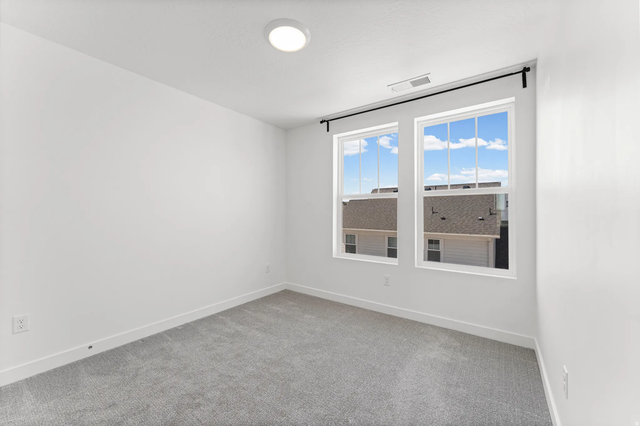Room featuring dual windows with white framing, gray carpeting, white walls, and a recessed ceiling light fixture