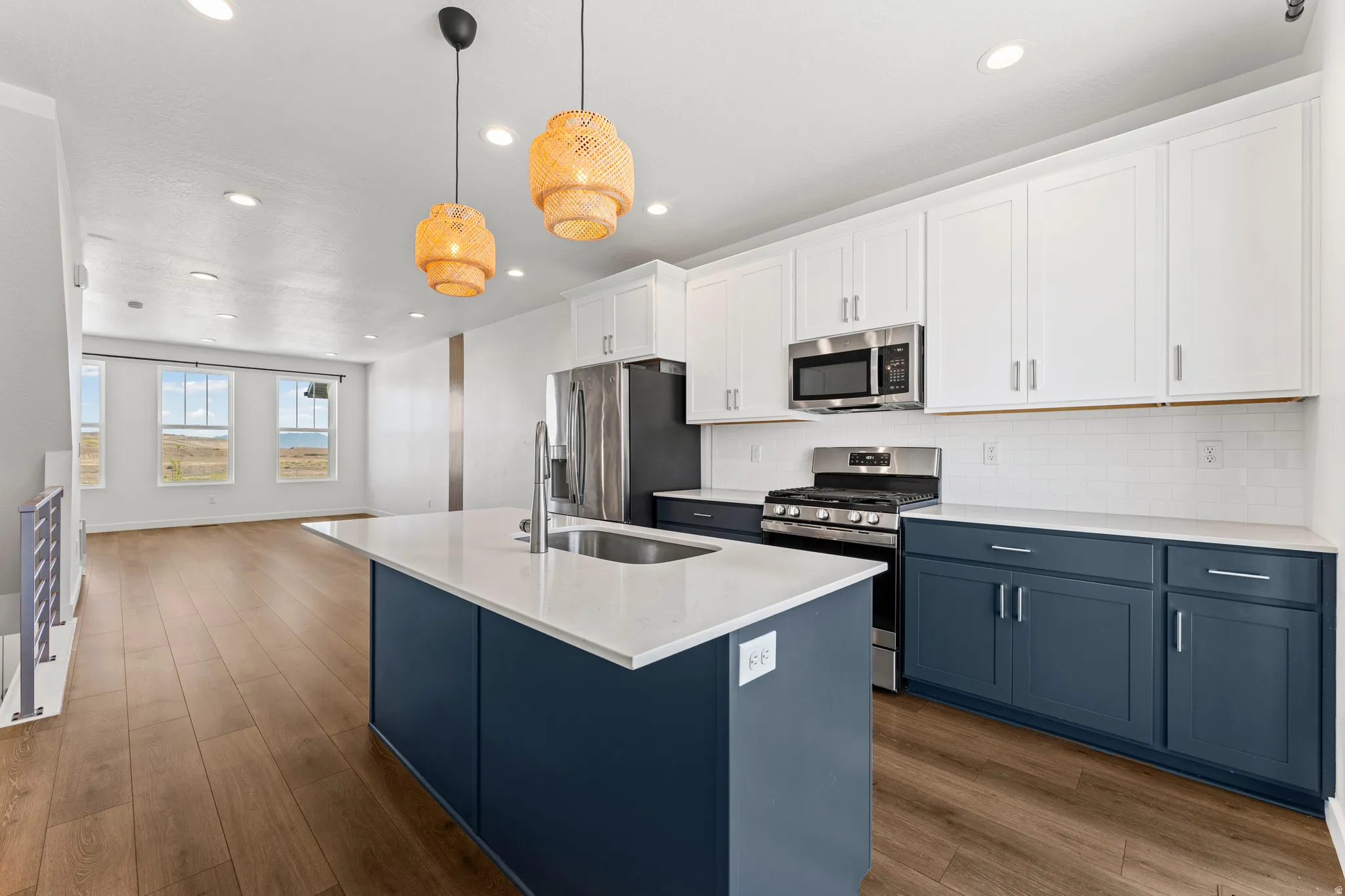 Open-concept kitchen featuring an island with an undermount sink, white quartz countertops, stainless steel appliances, and two-tone cabinetry with white upper and blue lower cabinets