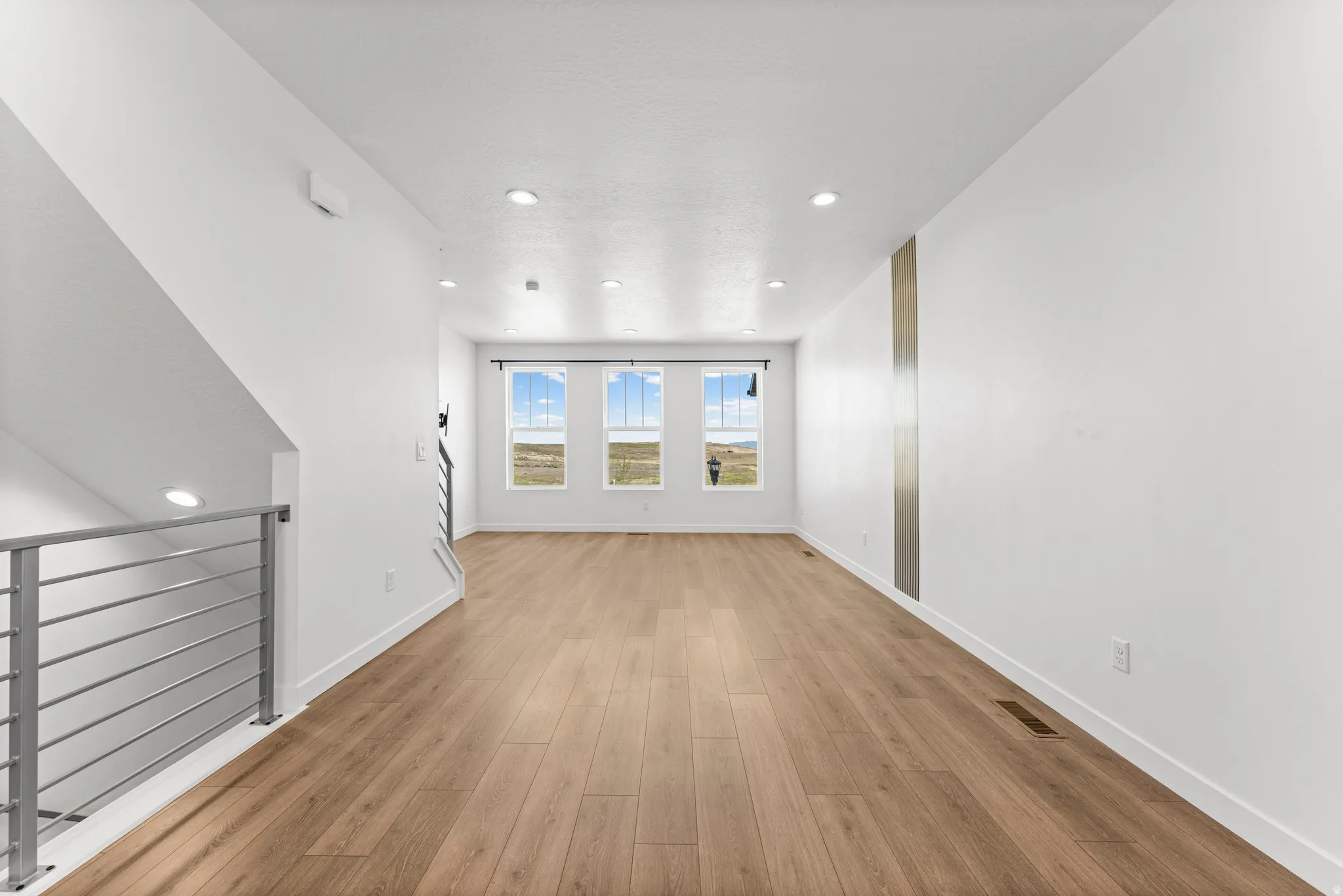 Open-concept room featuring wood-finish flooring, recessed lighting, and a modern horizontal bar railing