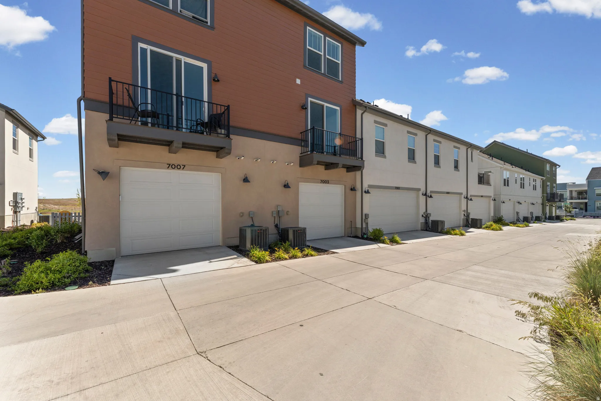 Contemporary townhome exterior featuring a private balcony, an attached garage, and light-toned stucco siding