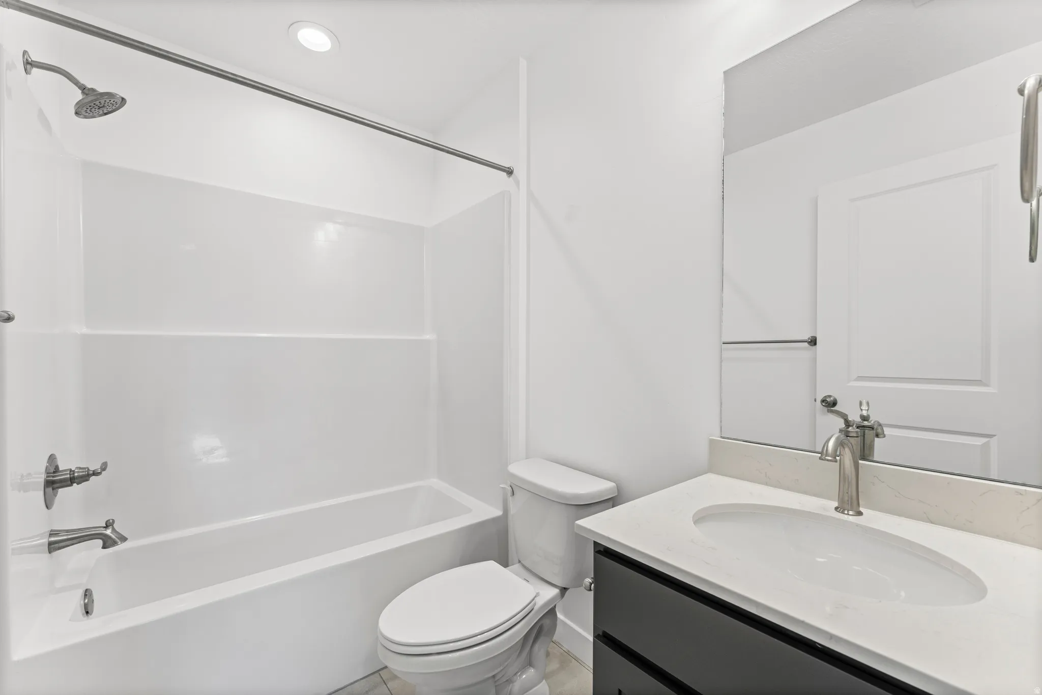 Bathroom featuring a white tub and shower surround with brushed nickel fixtures, a dark wood-finish vanity with a white countertop and integrated sink, a large wall-mounted mirror, and recessed lighting