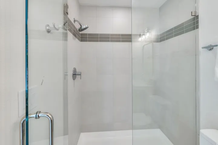 Glass-enclosed shower featuring a handheld showerhead and wall-mounted controls