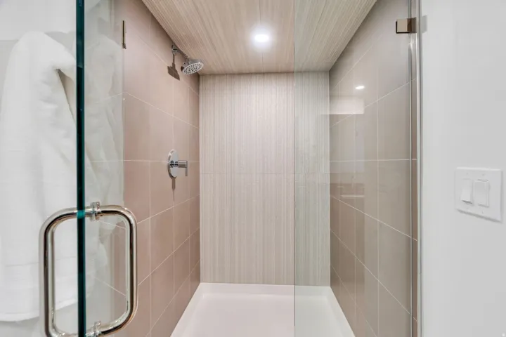 Glass-enclosed shower with ceramic tile walls, a wood-finish ceiling, and a bright overhead light