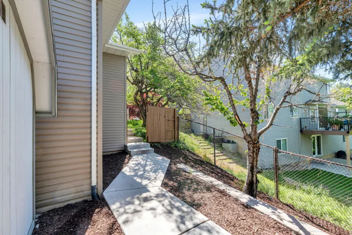 Concrete pathway leading to a wooden fence, bordered by a textured siding exterior and mulched landscaping