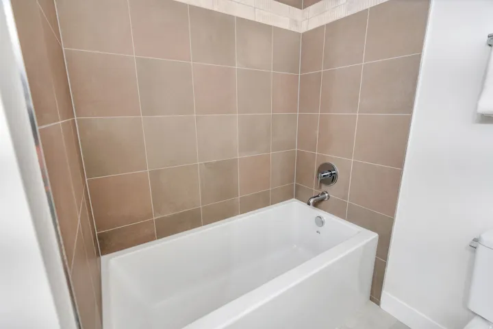 Bathtub and shower surround featuring neutral-toned square tiles with a decorative border