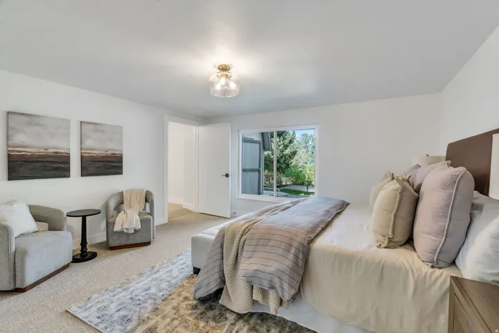 Carpeted bedroom featuring a window with exterior landscaping views, a ceiling-mounted light fixture, and white painted walls