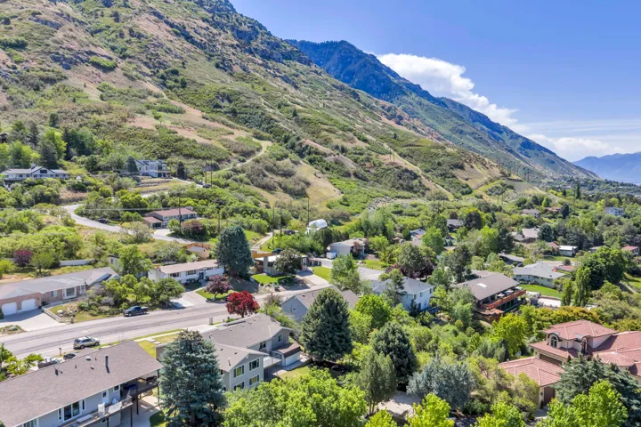 Residential area situated at the base of a verdant mountain range, featuring varied architectural styles and mature trees