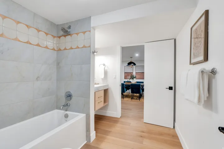 Full-sized bathtub with a chrome showerhead and faucet, surrounded by large format wall tiles and a decorative scalloped tile accent band