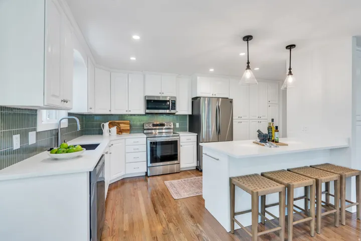 Modern kitchen featuring white cabinetry, a teal vertical tile backsplash, stainless steel appliances, a white countertop, and wood-finish flooring