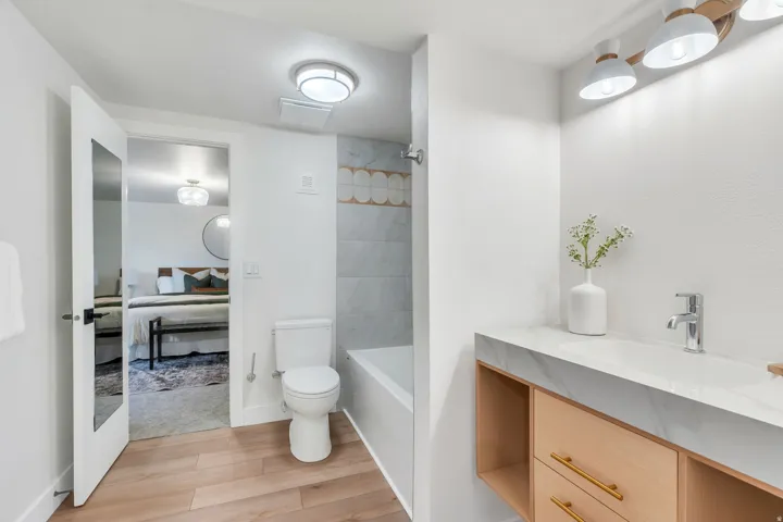 Full bathroom featuring wood-finish flooring, a contemporary vanity with a stone-finish countertop, a built-in bathtub with a tiled surround, and a modern light fixture