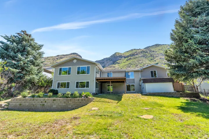 Multi-level residence featuring a rear elevated deck, ground-level patio, and a retaining wall with landscaping