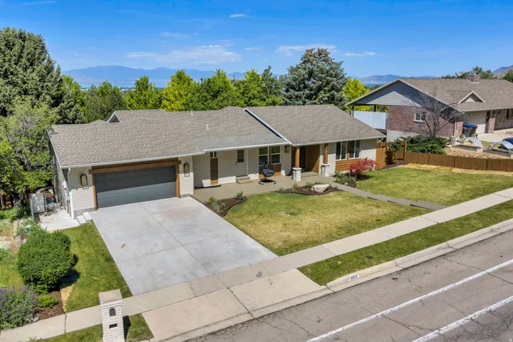 Ranch-style residence featuring a gray asphalt shingle roof, a two-car garage with a wood-look header, and a concrete driveway