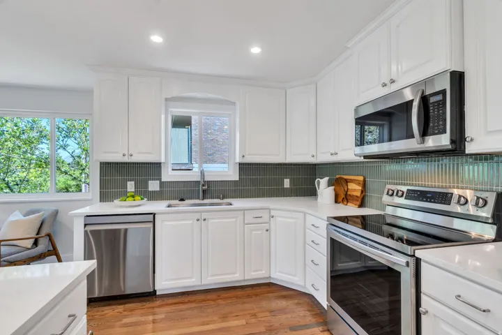Kitchen featuring white cabinetry, stainless steel appliances, a tile backsplash, light countertops, and wood-finish flooring