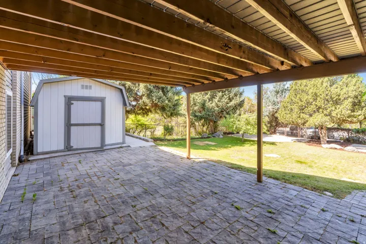 Covered patio featuring paver flooring, overhead wood beams, and structural support posts
