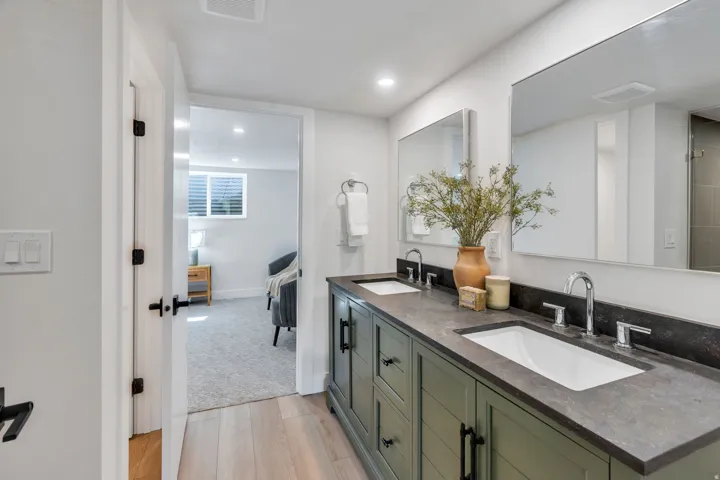 Dual vanity featuring a dark gray countertop, two undermount sinks with chrome fixtures, and a green wood-finish cabinet with black hardware