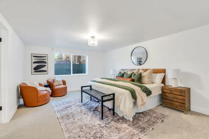 Bedroom featuring light-toned carpet flooring, a single window, white walls, a flush-mount ceiling light fixture, and a built-in wooden headboard