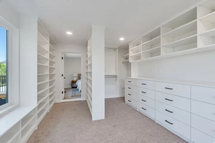 Spacious custom closet featuring extensive built-in shelving, integrated dresser drawers with black hardware, recessed lighting, and a neutral carpeted floor