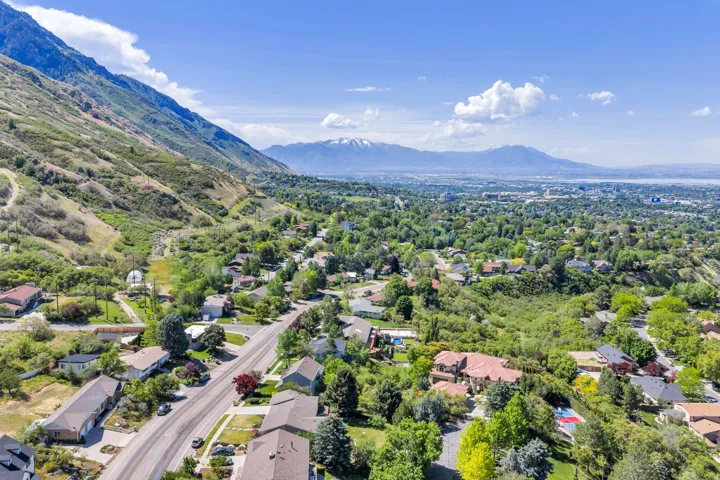 Aerial perspective showcasing a residential area nestled at the base of mountains, with a distant body of water and additional mountains on the horizon