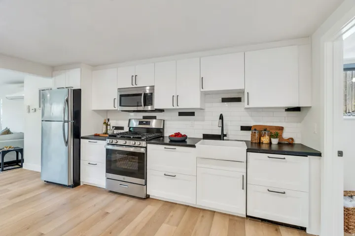 Modern kitchen featuring white shaker cabinetry, dark countertops, stainless steel appliances, a white subway tile backsplash with black accents, and wood-finish flooring