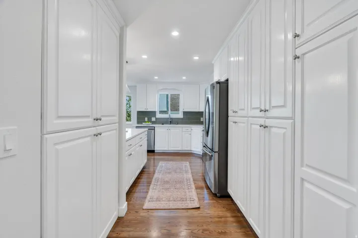 Kitchen featuring extensive white cabinetry with brushed nickel hardware, stainless steel refrigerator, recessed lighting, and wood-finish flooring