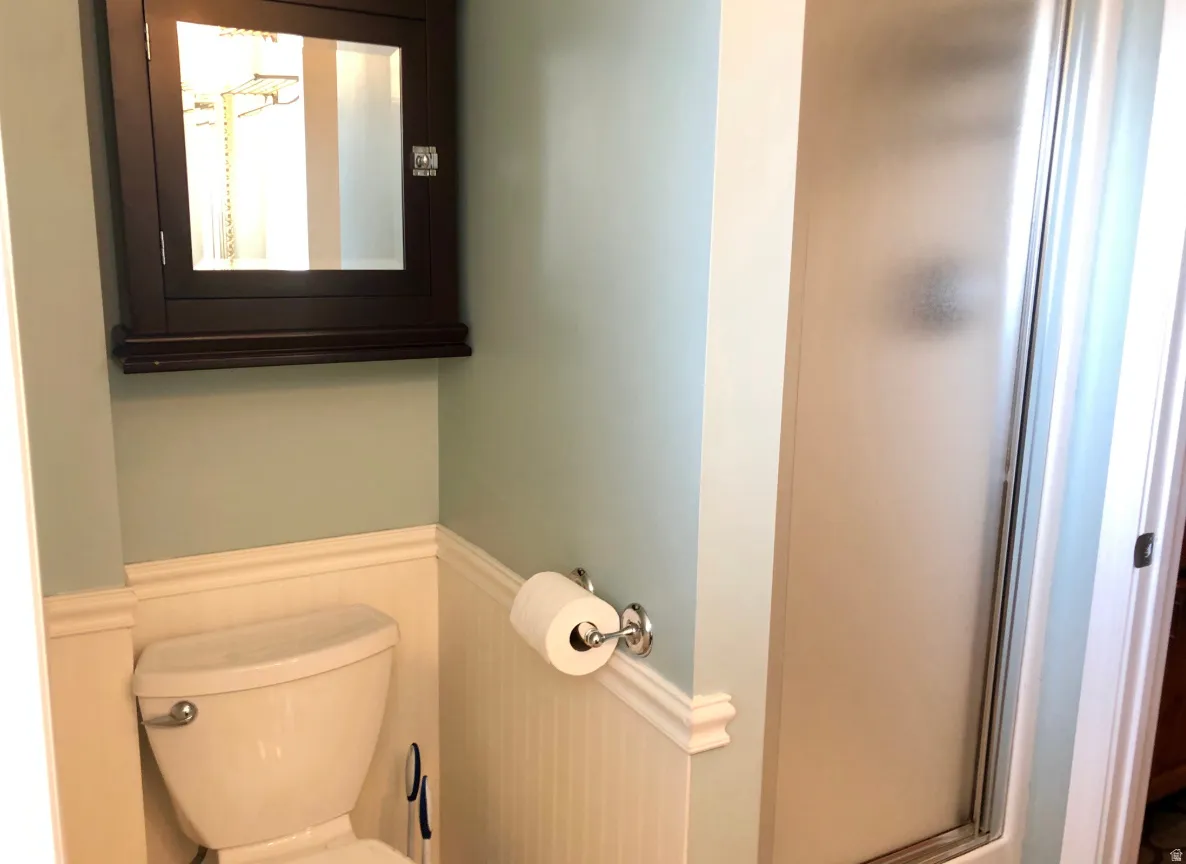 Bathroom featuring wainscoting, a wall-mounted medicine cabinet with a mirror, and a frosted glass shower enclosure