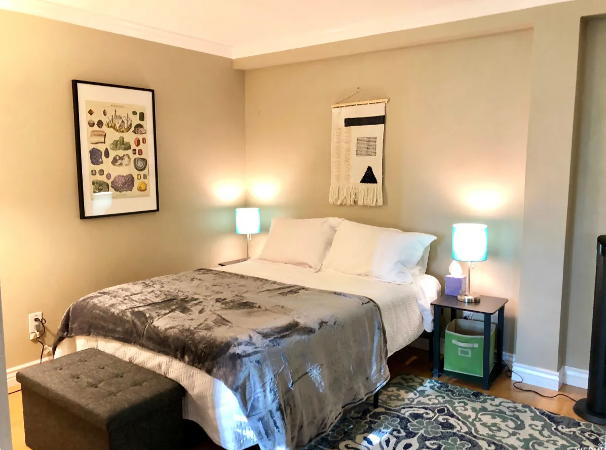 Bedroom featuring light beige walls, crown molding, and wood-finish flooring