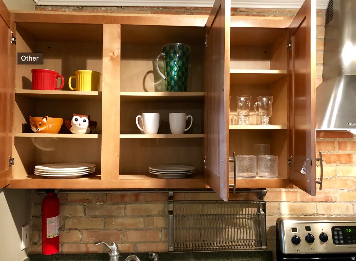 Wood-finish cabinetry with multiple shelving options, brick backsplash, stainless steel range hood, stainless steel stove, and a chrome kitchen faucet