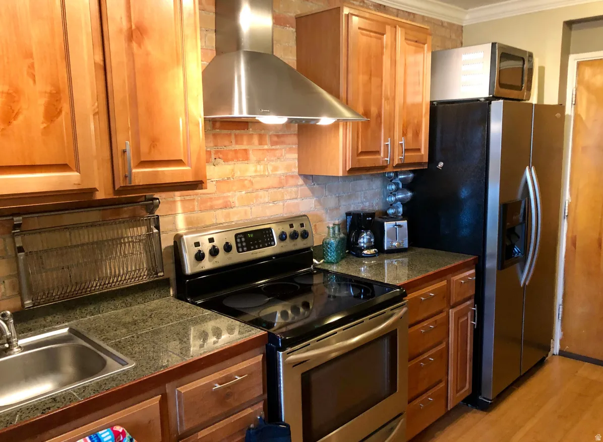 Kitchen featuring natural wood cabinetry, stainless steel appliances, brick-style backsplash, and granite-look countertops