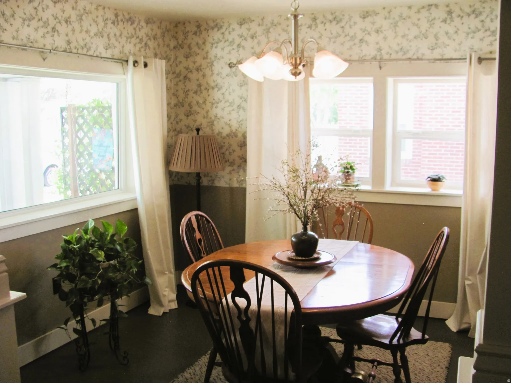 Dining area featuring dark wood-finish flooring, patterned wallpaper, a central chandelier, and multiple windows with white trim
