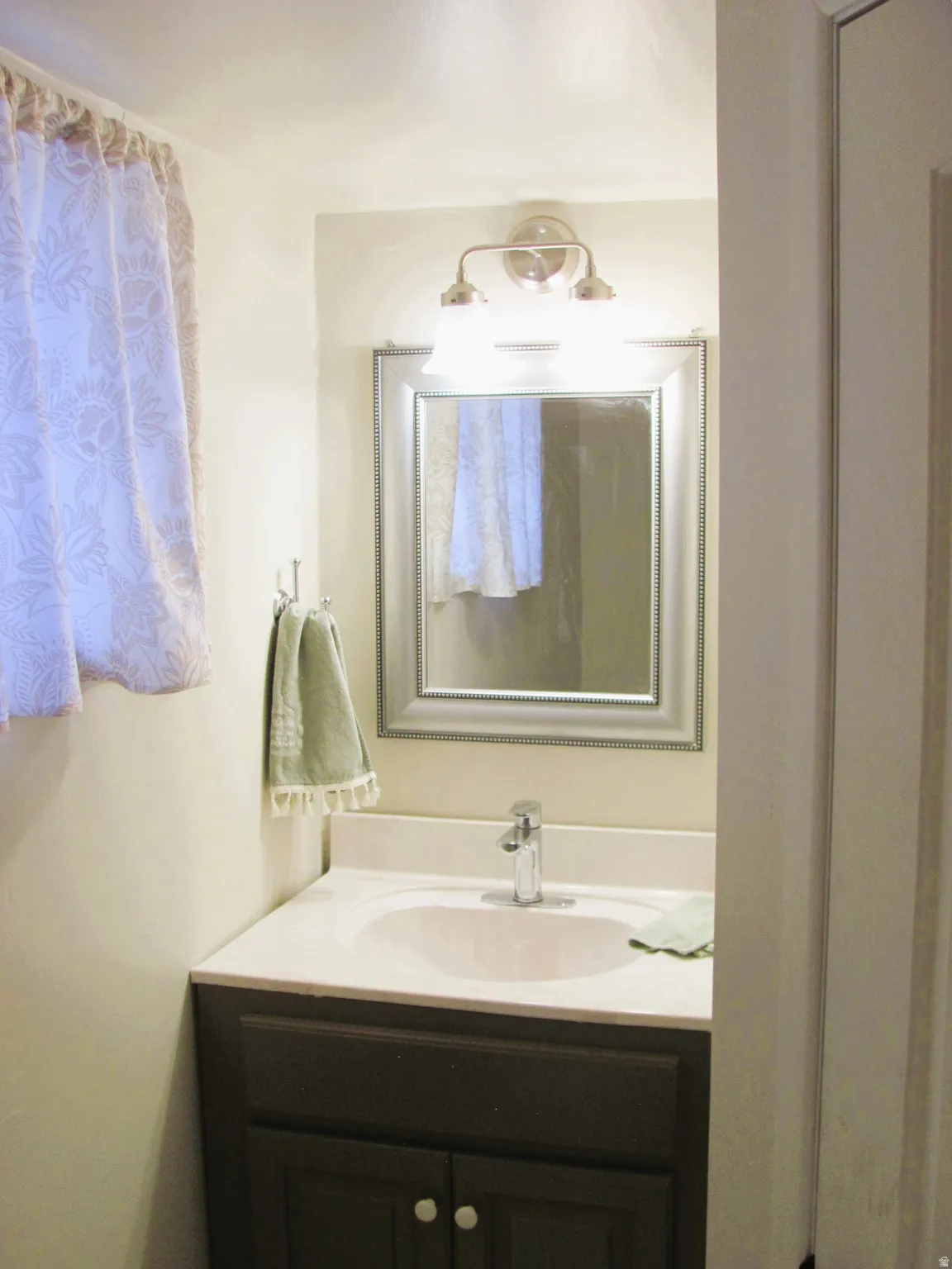 Bathroom vanity featuring a white countertop with an integrated sink, a dark wood-finish cabinet, and a chrome faucet