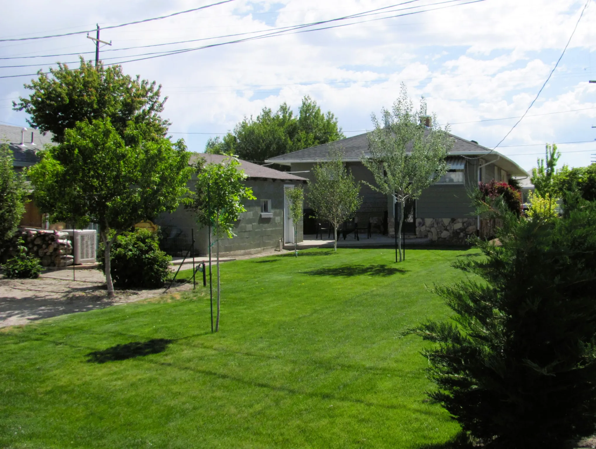 Expansive green lawn with mature trees, a detached auxiliary structure, and a main residence featuring a stone foundation and siding
