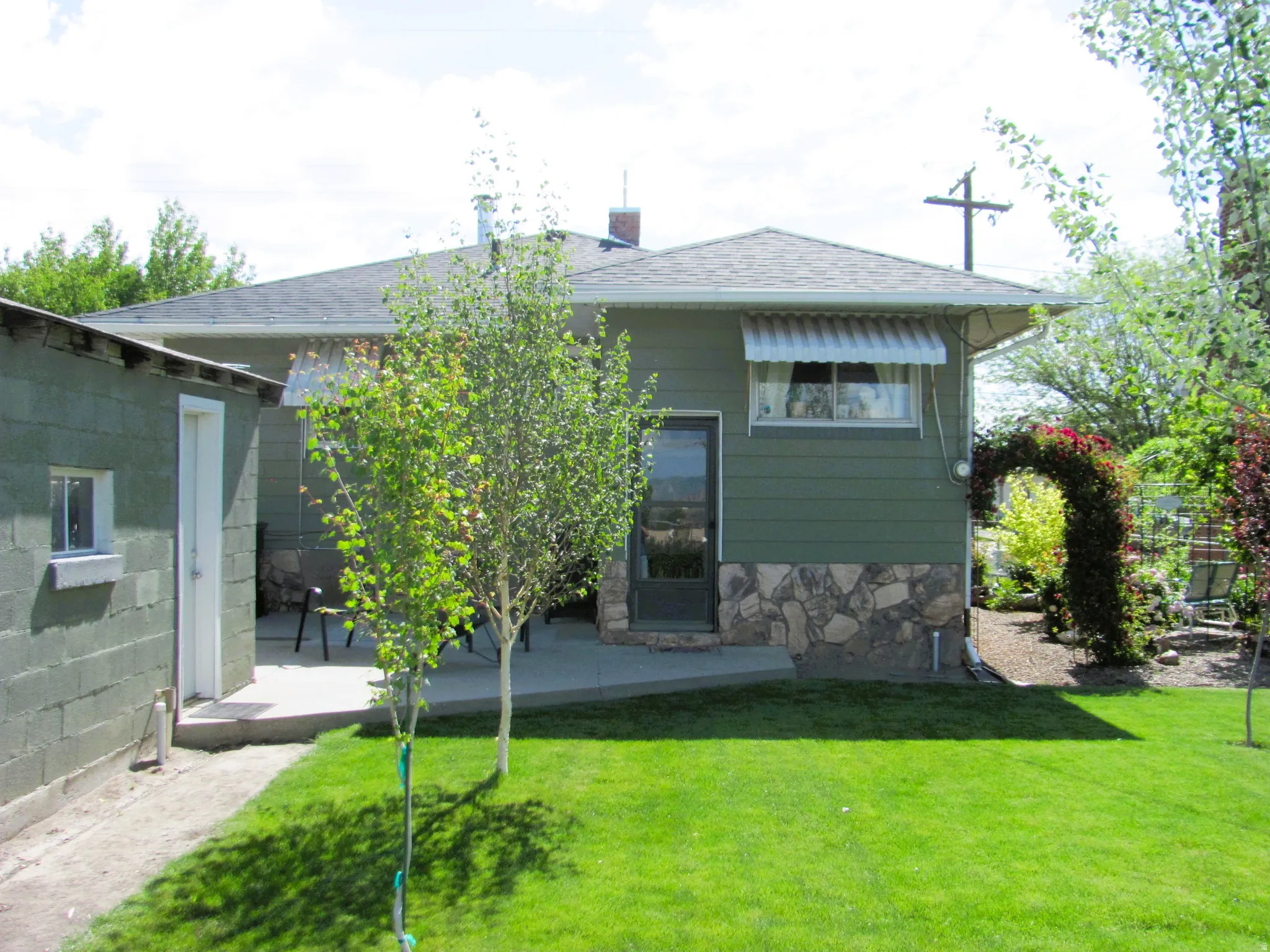 Rear exterior with a concrete patio, stone veneer accents, and a green lawn