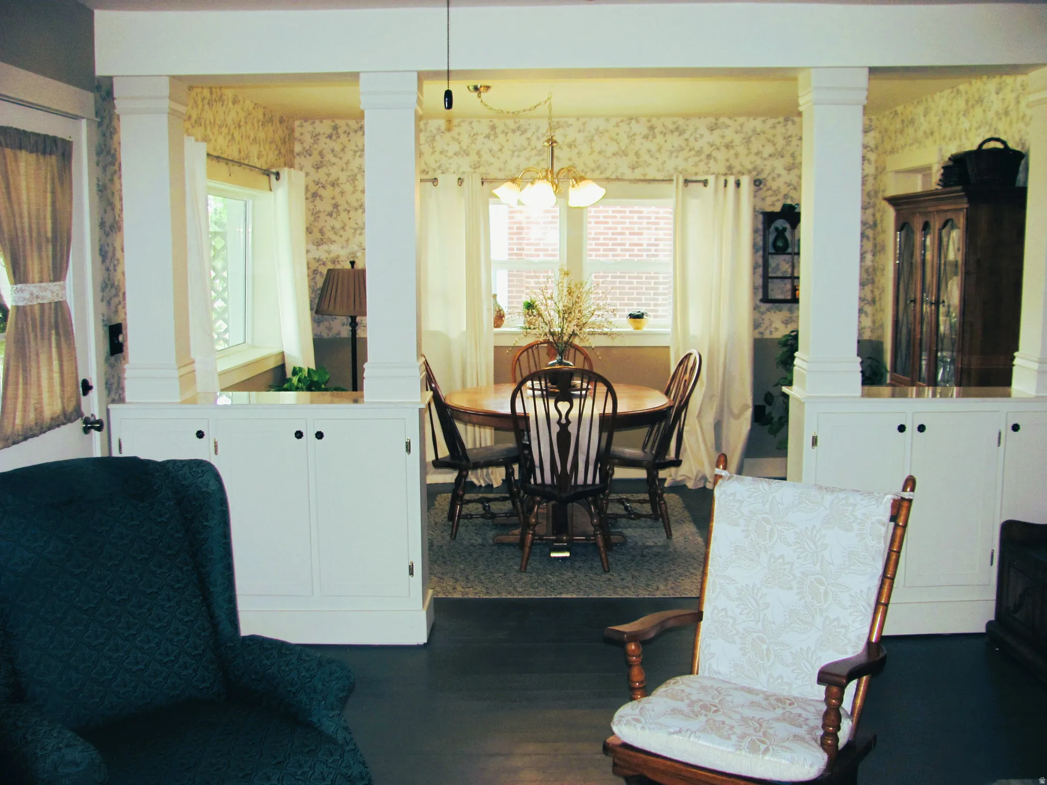 Columned entryway featuring built-in cabinetry, dark wood-finish flooring, and a dining area with a brass chandelier