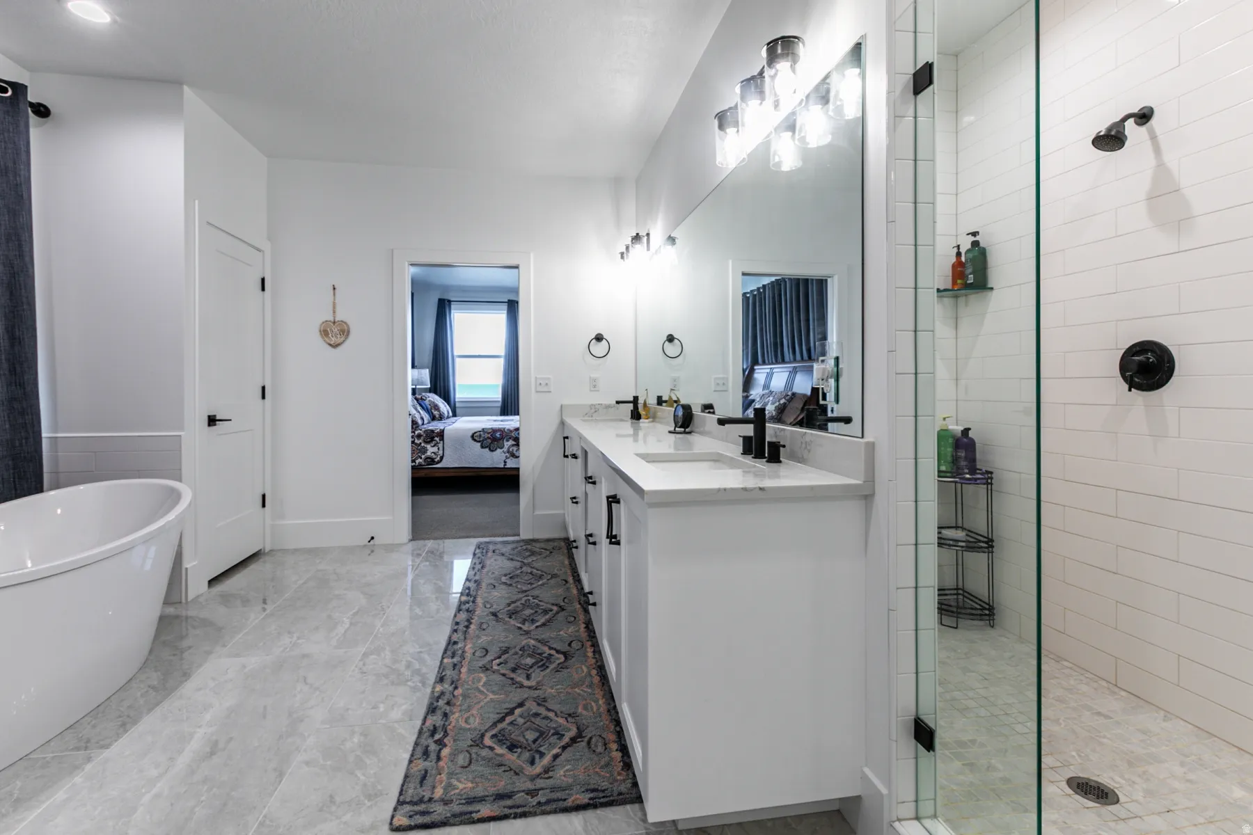 Contemporary bathroom featuring a freestanding tub, dual vanity with undermount sinks and black fixtures, and a glass-enclosed shower with subway tile surround