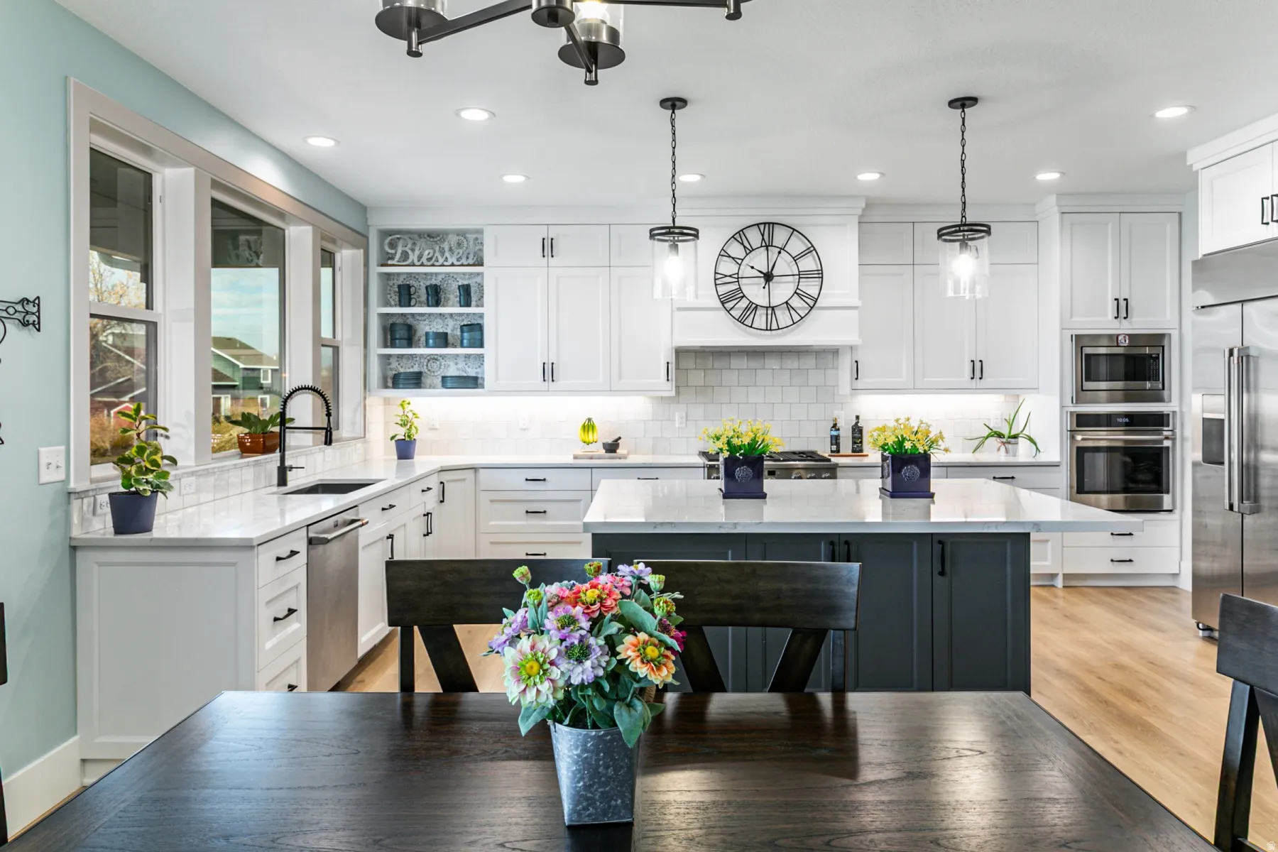 Open-concept kitchen featuring white shaker-style cabinetry, a contrasting dark gray island with a light-toned countertop, stainless steel appliances, and wood-finish flooring