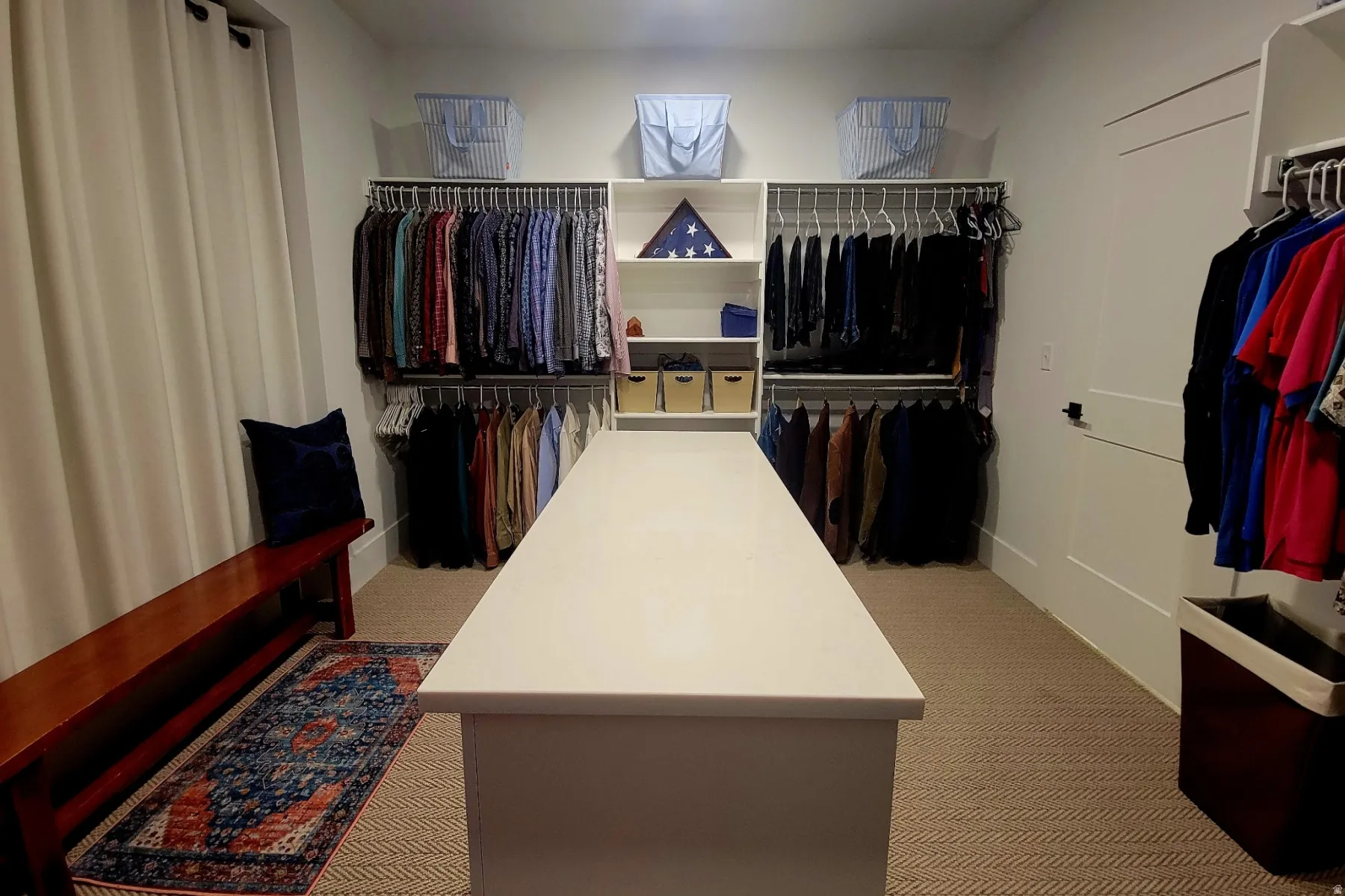 Custom closet system featuring a central island with a solid surface countertop, multiple hanging rods, integrated shelving, and neutral tone carpeting