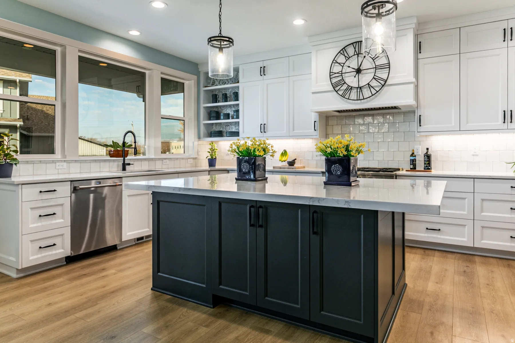 Expansive kitchen featuring a large central island with dark cabinetry and light-toned countertops, white perimeter cabinetry, wood-finish flooring, and a white subway tile backsplash