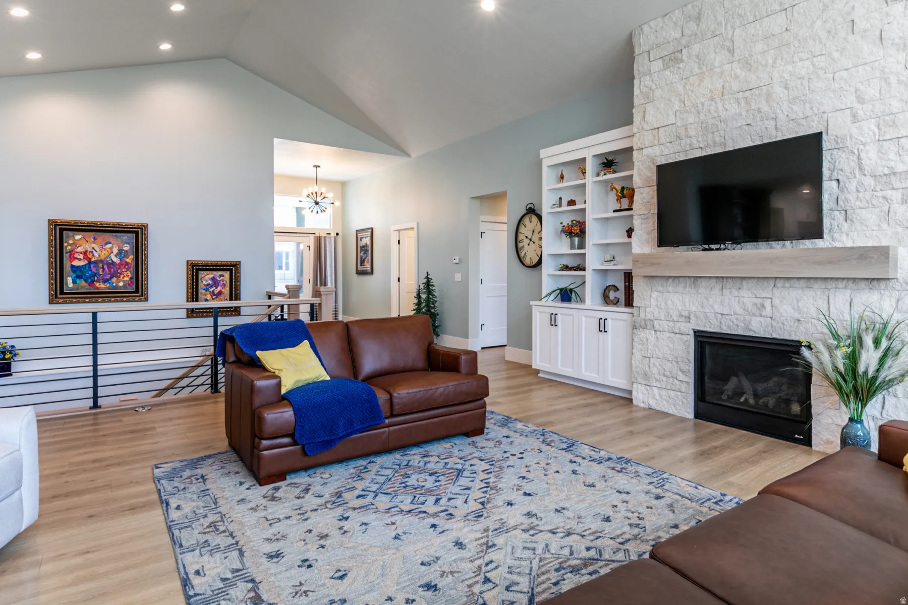 Spacious living area featuring a vaulted ceiling with recessed lighting, stone-clad fireplace with mantel, built-in shelving, and wood-finish flooring