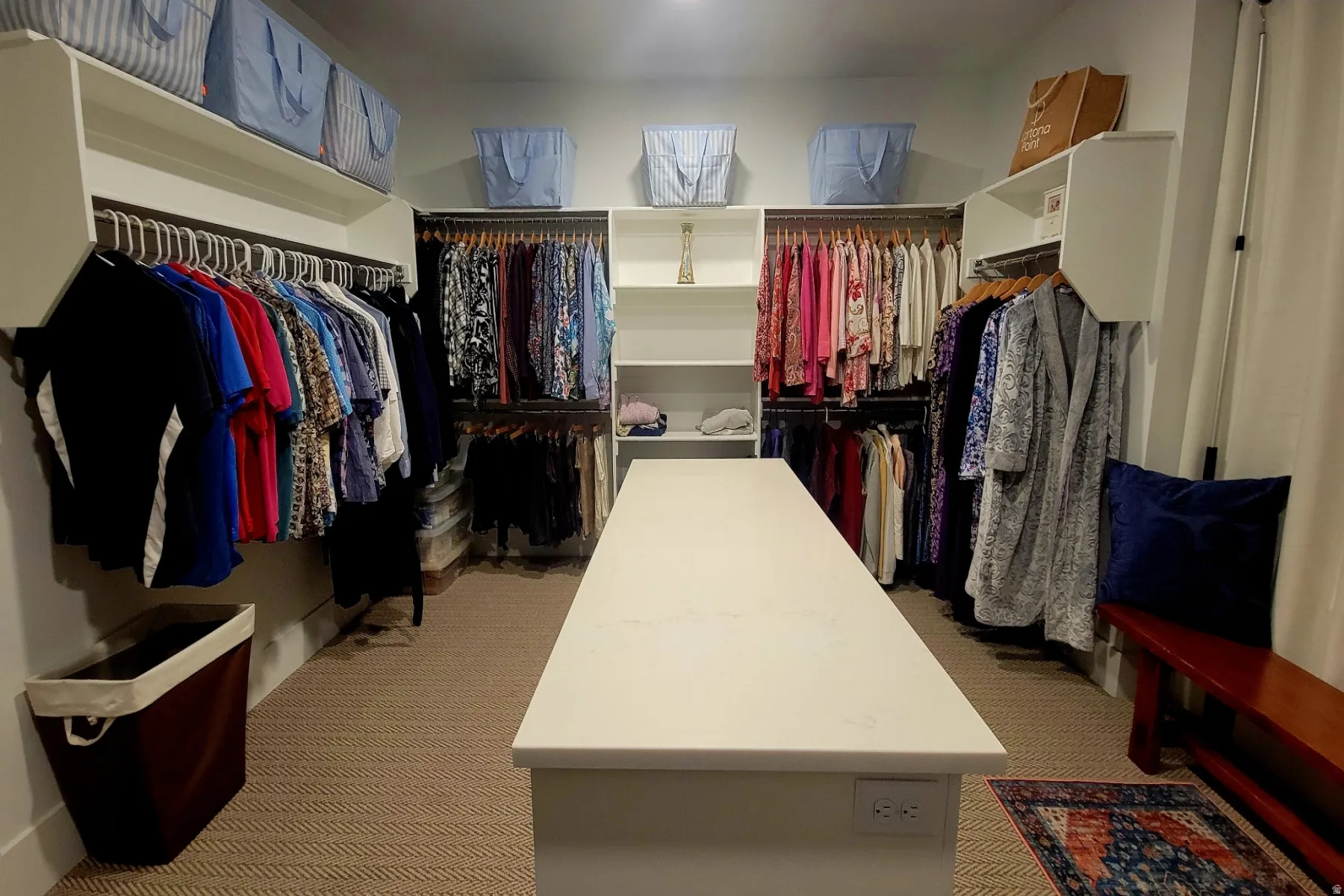 Spacious walk-in closet featuring extensive built-in shelving, multiple hanging rods, and a central island with a solid surface countertop