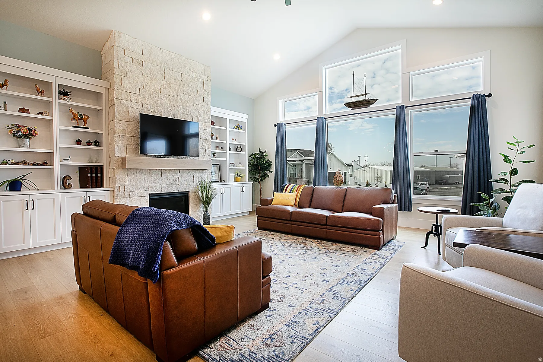 Vaulted living room featuring a stone-clad fireplace with a hearth, custom built-in shelving, wood-finish flooring, and multiple transom windows