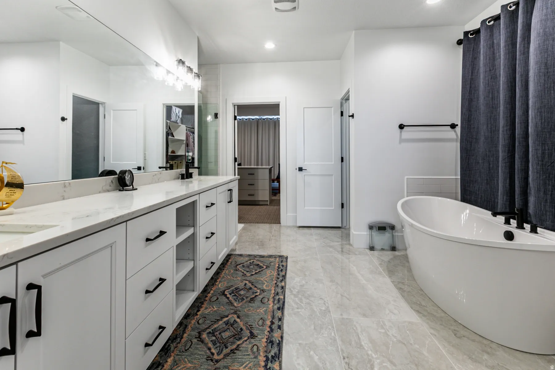 Spacious bathroom featuring a freestanding soaking tub, an extended vanity with white cabinetry, light-toned countertops, and large format floor tiling