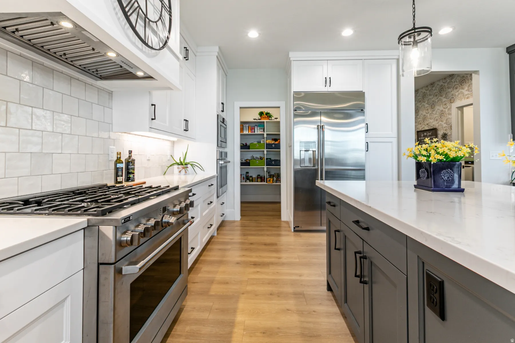 Gourmet kitchen featuring a stainless steel range with overhead ventilation, white shaker cabinetry, light-toned countertops, a stainless steel refrigerator, and wood-finish flooring