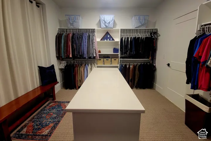 Custom closet system featuring a central island with a solid surface countertop, multiple hanging rods, integrated shelving, and neutral tone carpeting