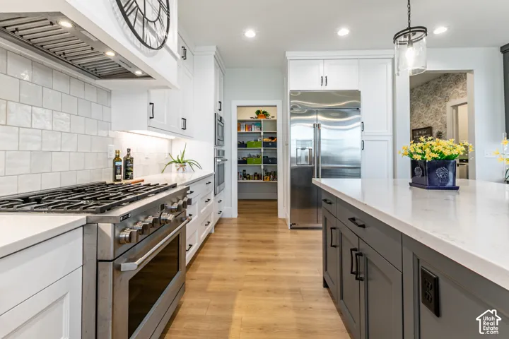 Gourmet kitchen featuring a stainless steel range with overhead ventilation, white shaker cabinetry, light-toned countertops, a stainless steel refrigerator, and wood-finish flooring