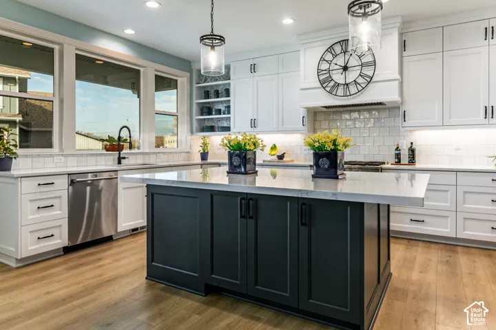 Expansive kitchen featuring a large central island with dark cabinetry and light-toned countertops, white perimeter cabinetry, wood-finish flooring, and a white subway tile backsplash